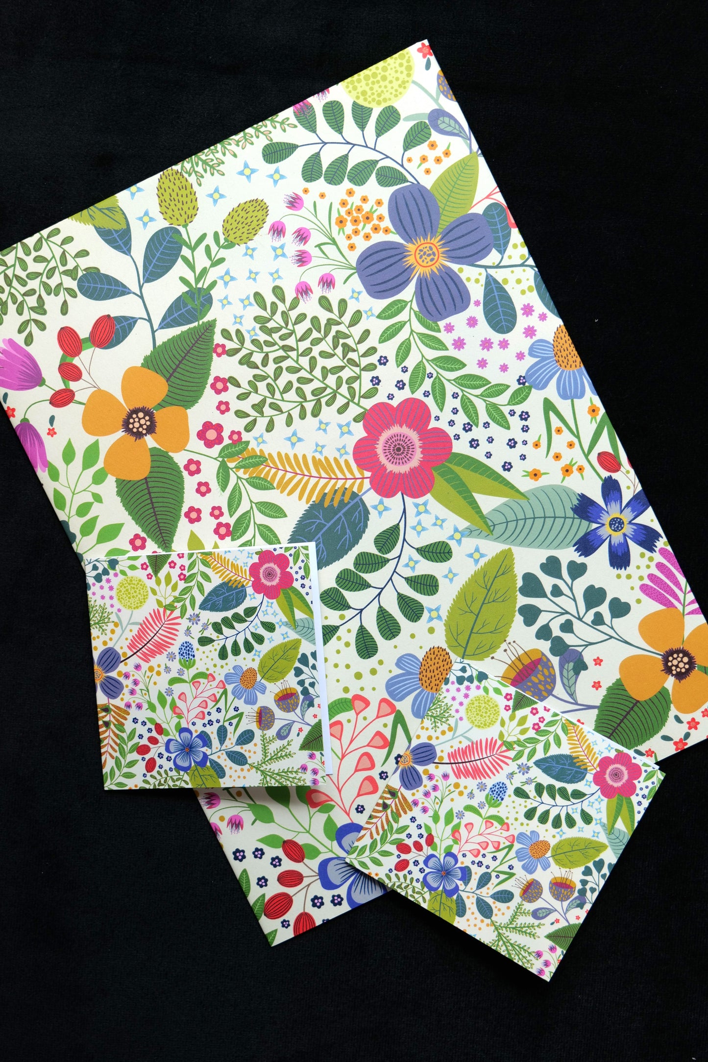 A folded piece of gift wrap and two small gift cards featuring the bright Spring Garden design, displayed against a black background