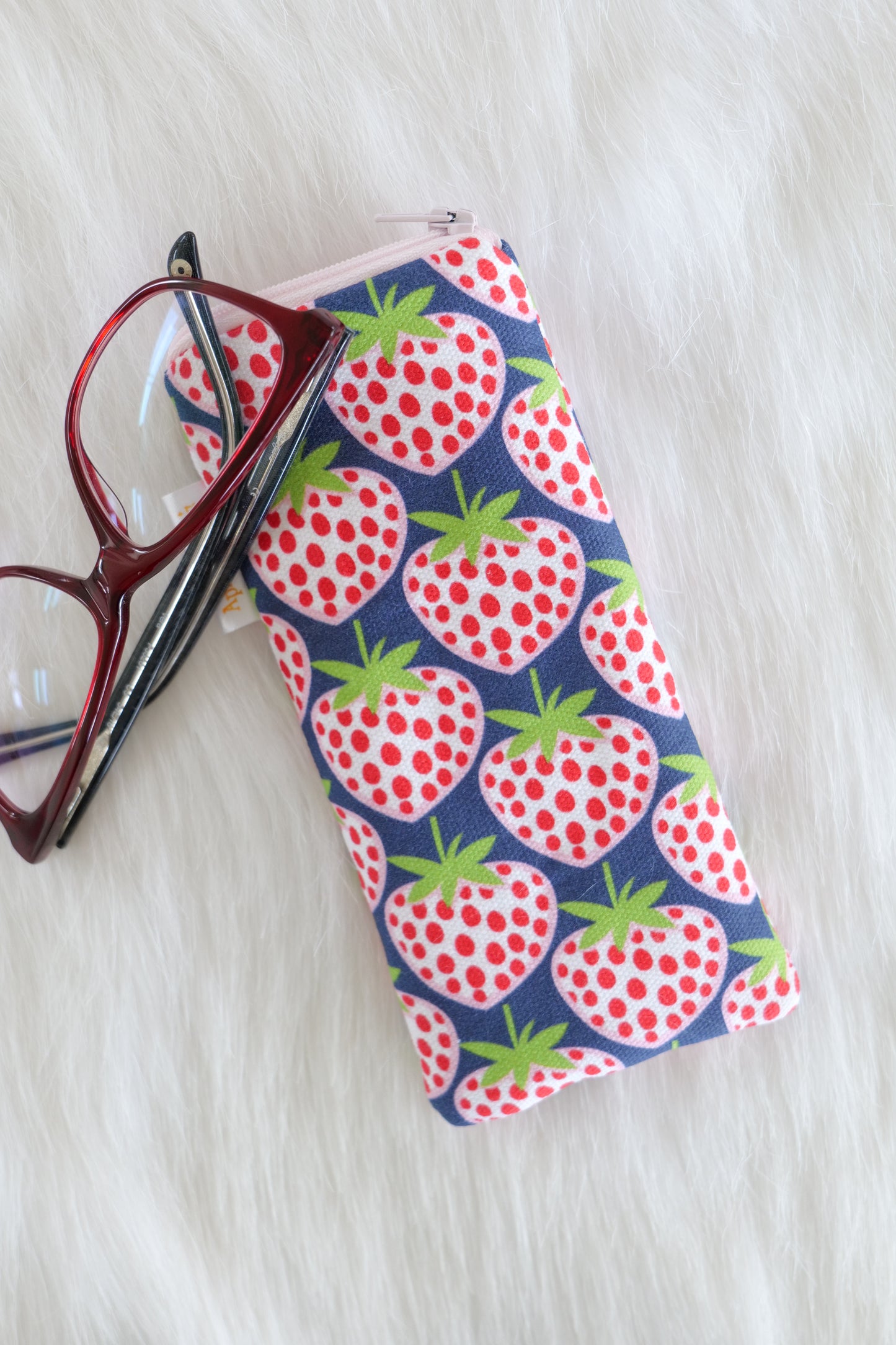 Blue strawberry patterned glasses case made from cotton canvas with zip top closure, padded and lined with soft cotton, displayed on a white background alongside a pair of eyeglasses. Handmade in Melbourne and certified Australian Made.