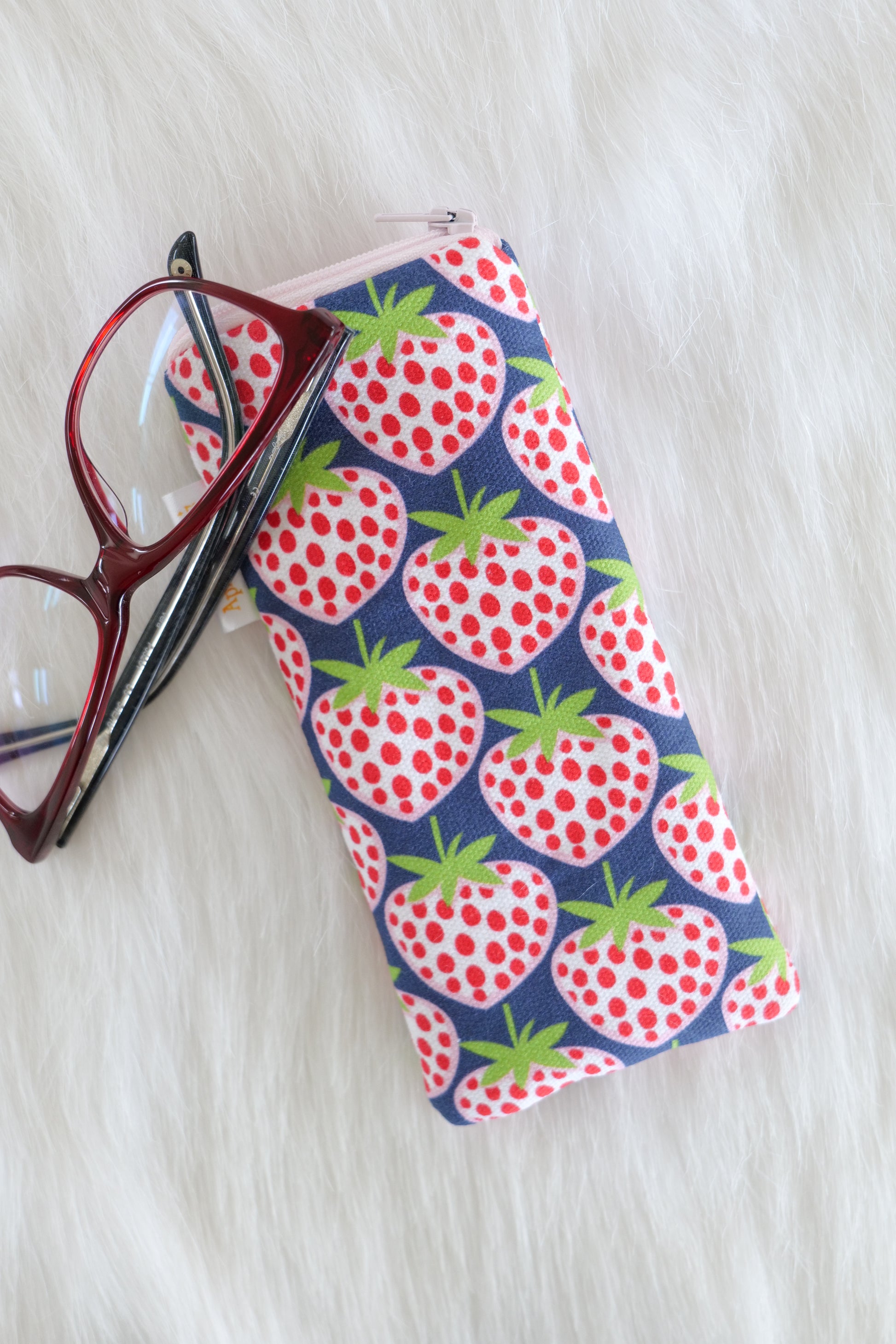 Blue strawberry patterned glasses case made from cotton canvas with zip top closure, padded and lined with soft cotton, displayed on a white background alongside a pair of eyeglasses. Handmade in Melbourne and certified Australian Made.