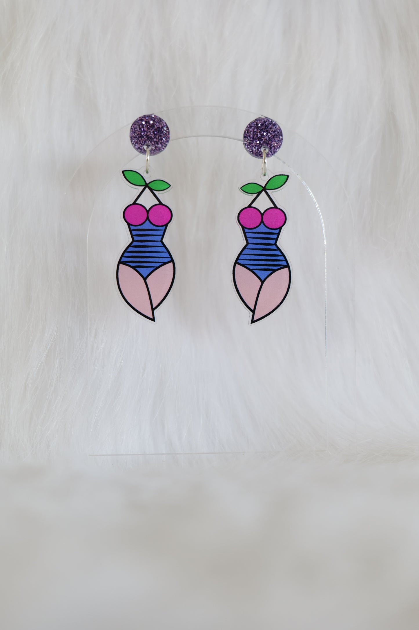 Fun pair of lightweight acrylic earrings in the shape of a female torso and thighs, wearing a striped blue swimsuit with boobs made from a pair of cherries and leaves as the halter neck, mauve glitter stud at the top, stainless steel posts and large accessible backs, displayed against a white background