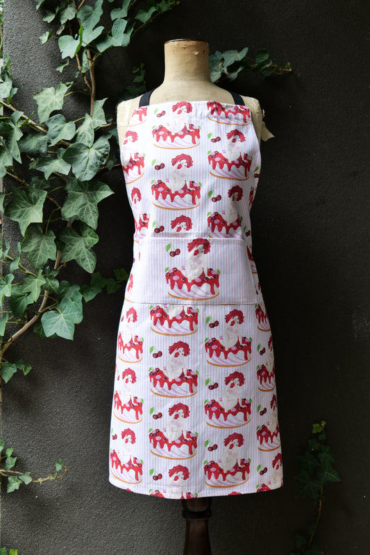 Cake Nude apron features voluptuous nude women reclining on a cake on a background of pink stripes, modelled on a mannequin set against a dark background; apron has extended waist ties and adjustable neck, made from cotton canvas, machine washable and Australian made