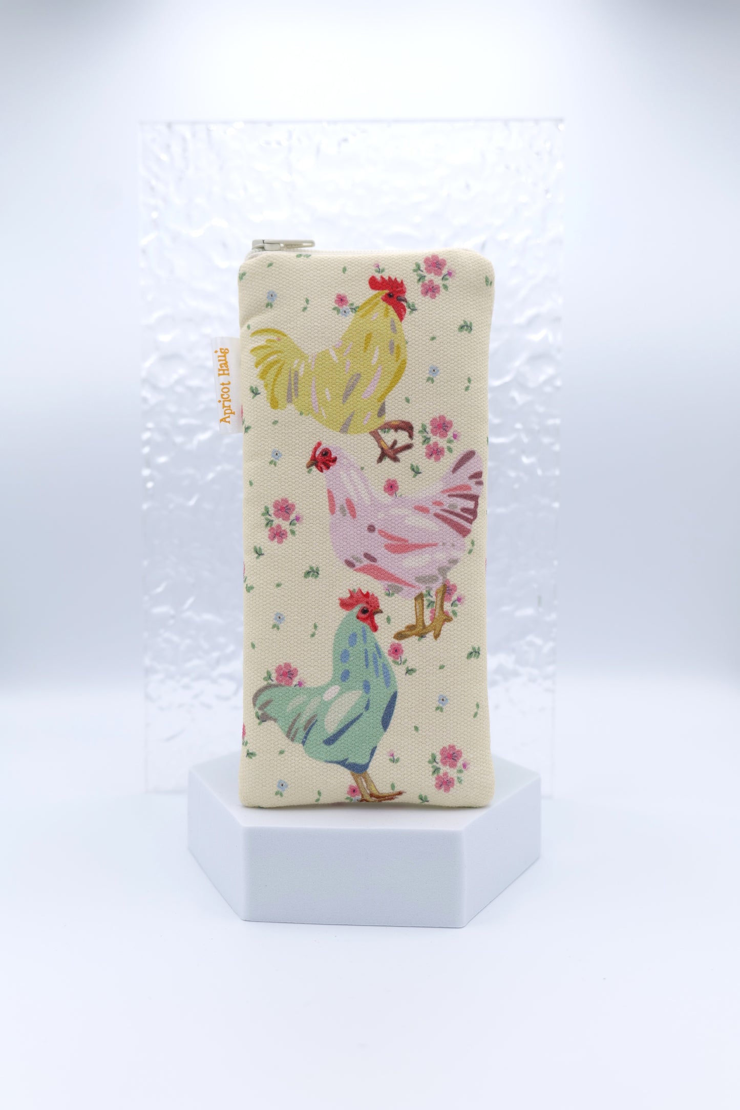 Glasses case featuring Chooks design with three colourful chickens stacked vertically — yellow, pink, and teal — surrounded by small pink florals on a cream background; made from cotton canvas with a zip-top closure, padded and lined to protect lenses, handmade in Melbourne and certified Australian Made; matching apron and tea towel available; pattern placement may vary slightly due to the handmade nature of the product.