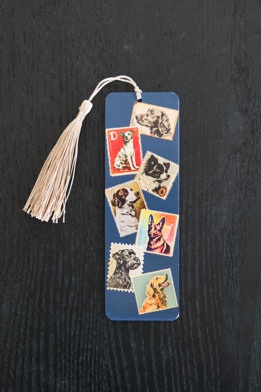 Bookmark featuring stamps with different dogs on a dark blue background with a gold tassel; sitting against a black backdrop