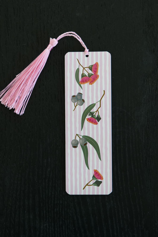 Bookmark featuring eucalyptus blossoms, gumnuts and leaves on a pink and white striped background with a pale pink tassel, sitting against a black backdrop