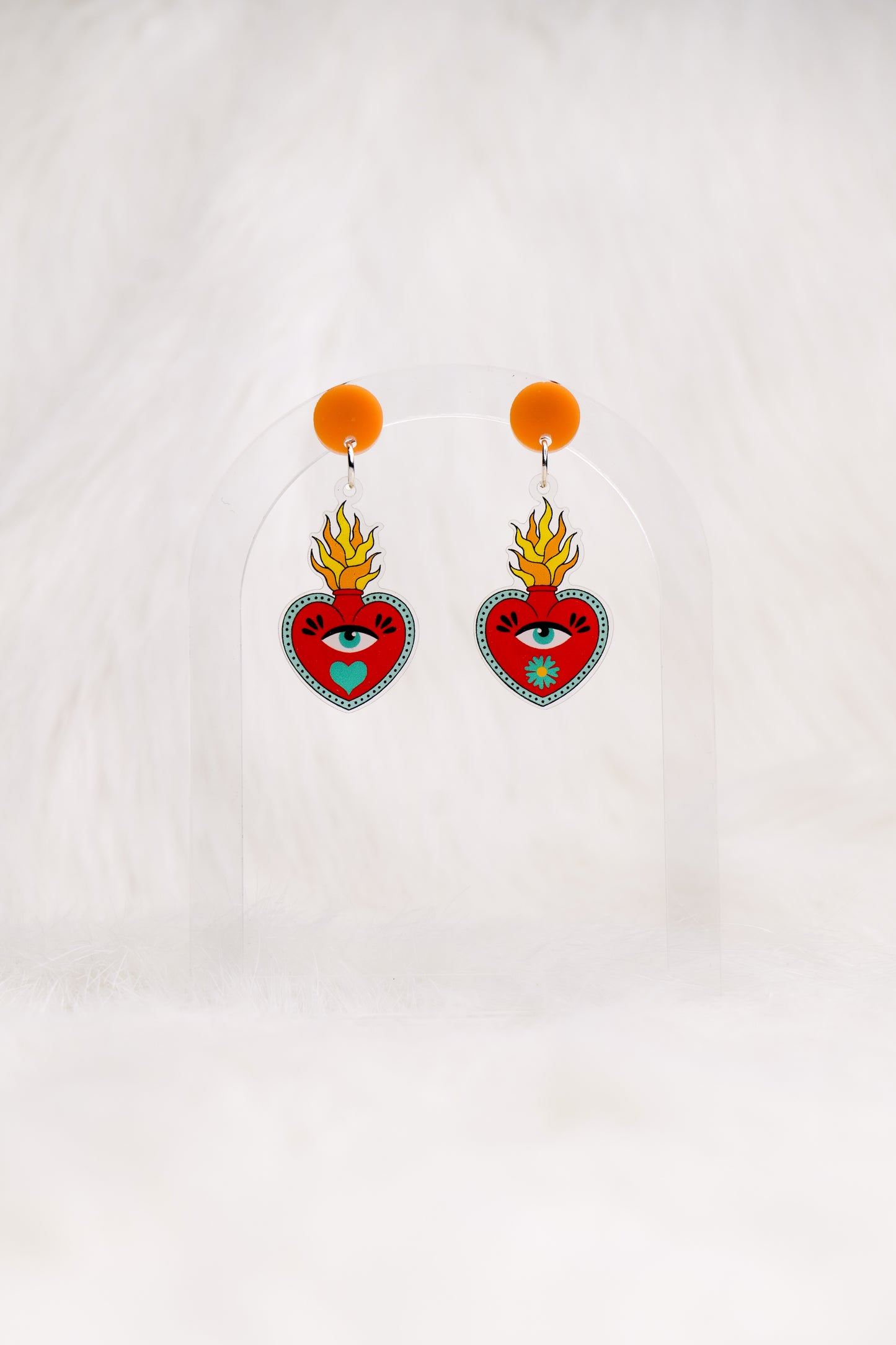 Heart-shaped red earrings with an eye and a flame out the top, printed on acrylic with a circular orange top and stainless steel posts with large accessible backs, earrings shown against a white background