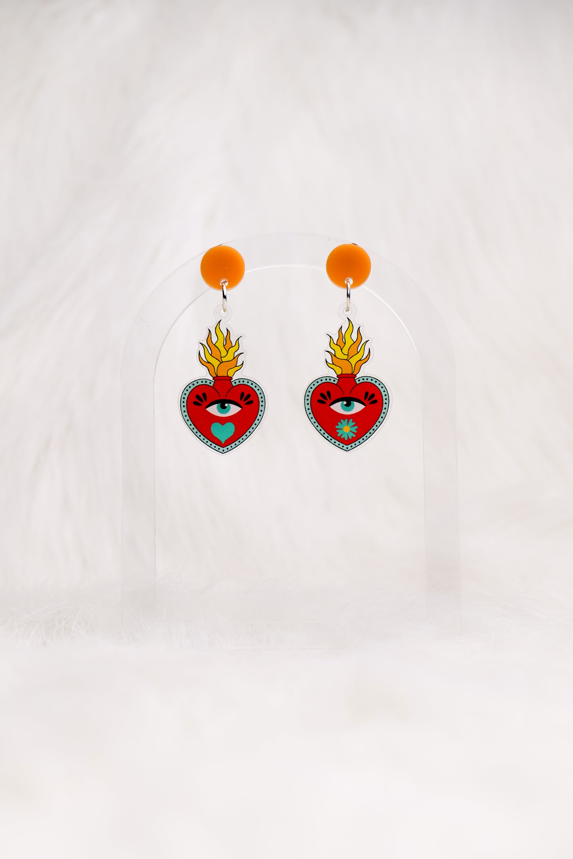 Heart-shaped red earrings with an eye and a flame out the top, printed on acrylic with a circular orange top and stainless steel posts with large accessible backs, earrings shown against a white background