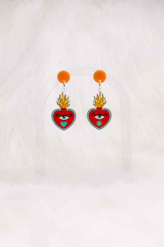 Heart-shaped red earrings with an eye and a flame out the top, printed on acrylic with a circular orange top and stainless steel posts with large accessible backs, earrings shown against a white background