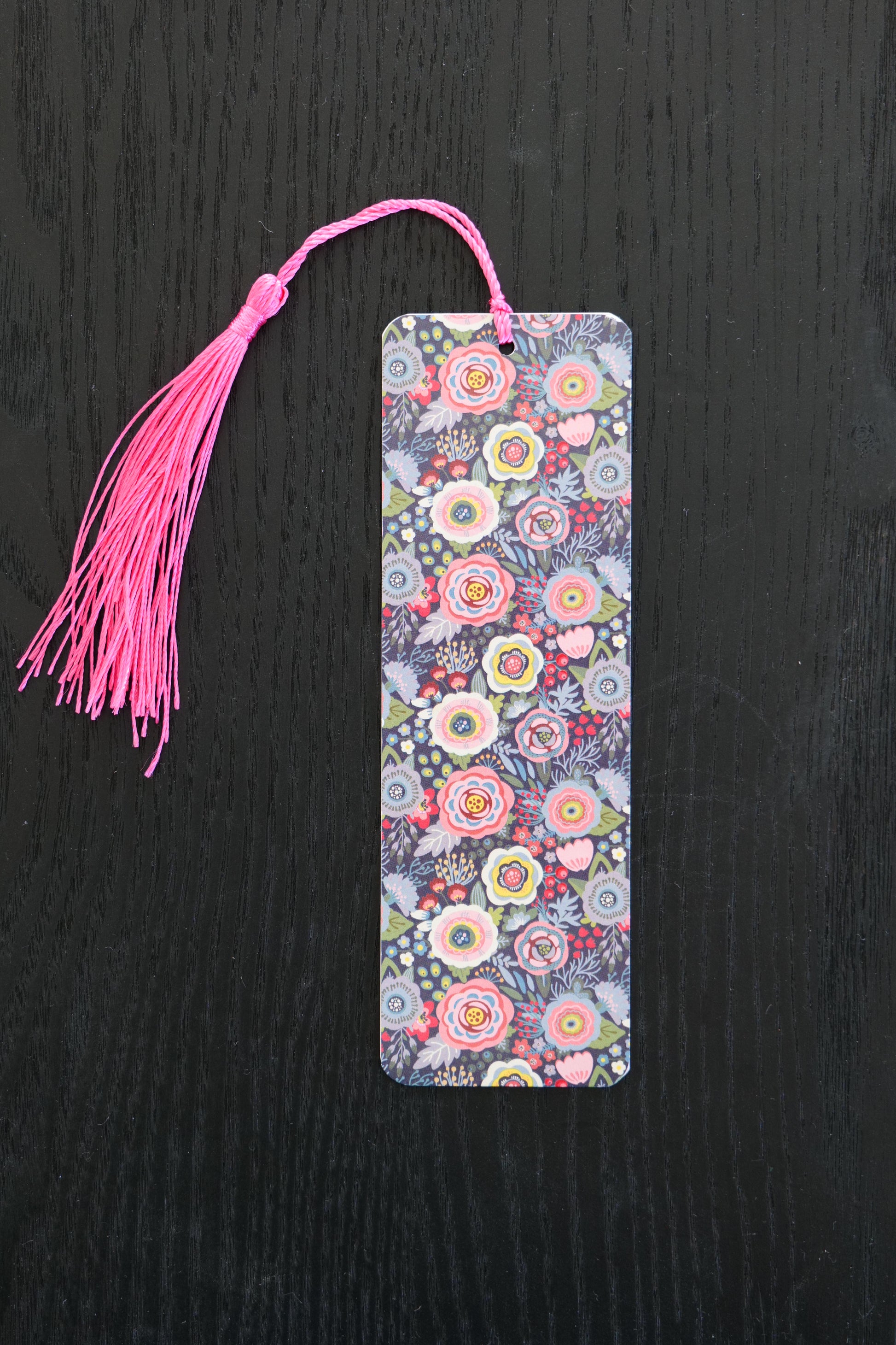 Bookmark with a grey and pink floral design, with a pink tassel, sitting against a black background