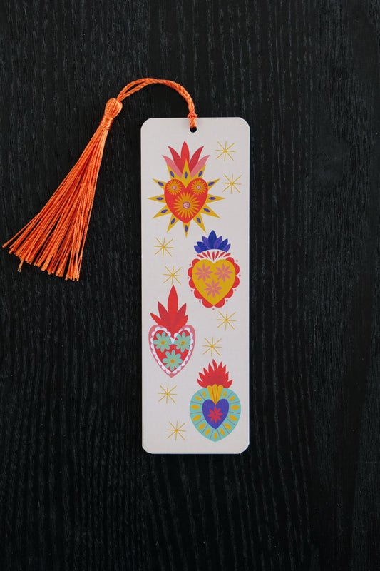 Bookmark with four colourful hearts with patterns and flames at the top, with a pale pink background and yellow stars and an orange tassel, sitting against a black backdrop