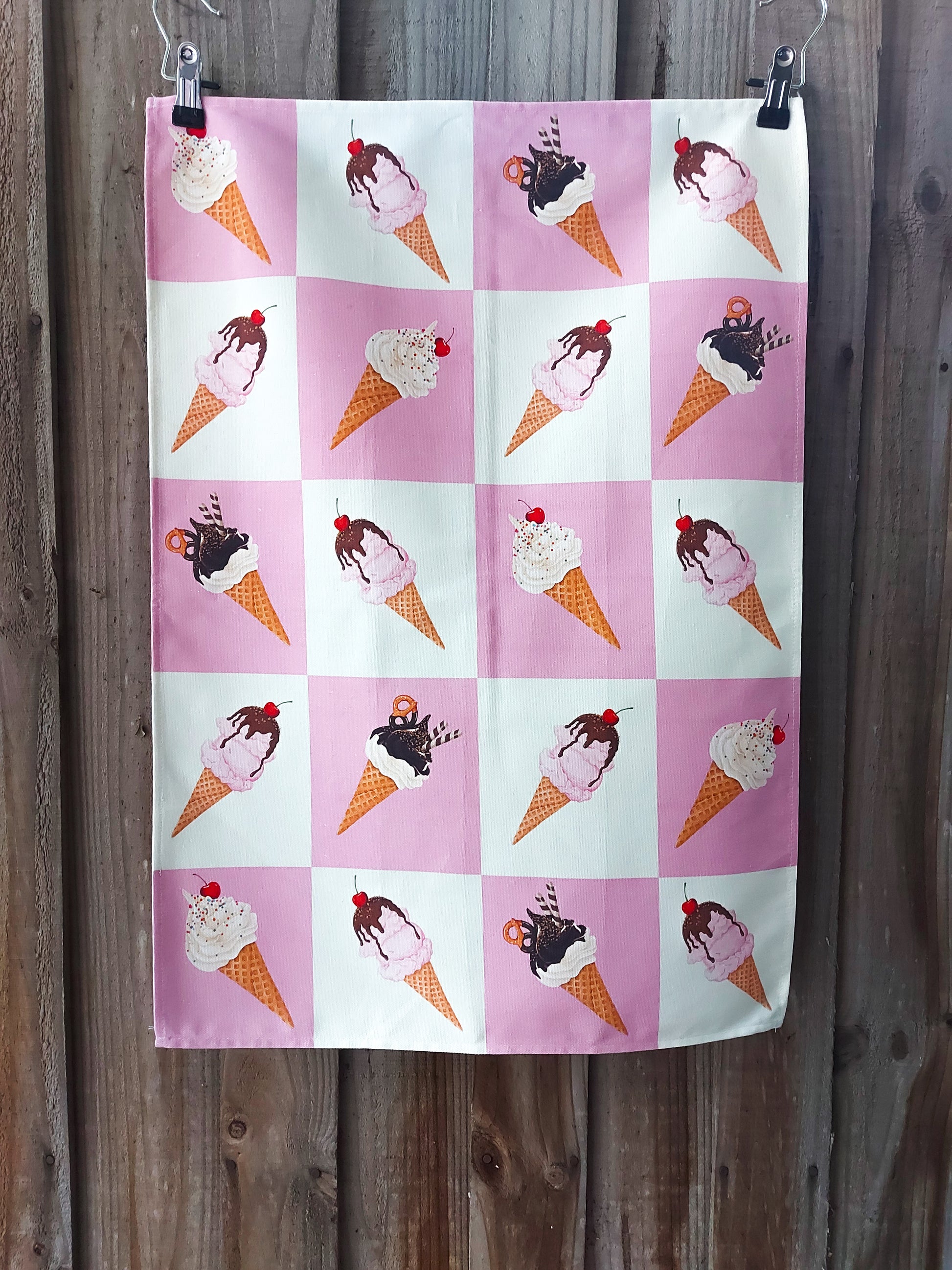 100% cotton tea towel featuring a repeating grid of illustrated ice‑cream cones on alternating pink and white squares; displayed against a wooden fence