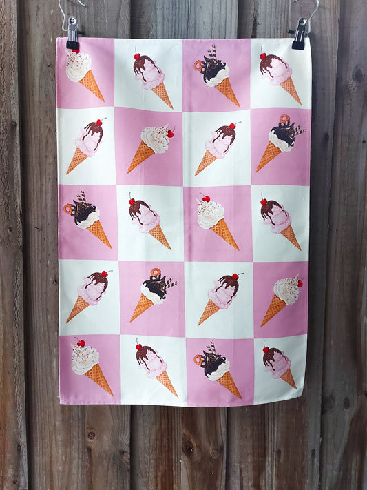 100% cotton tea towel featuring a repeating grid of illustrated ice‑cream cones on alternating pink and white squares; displayed against a wooden fence