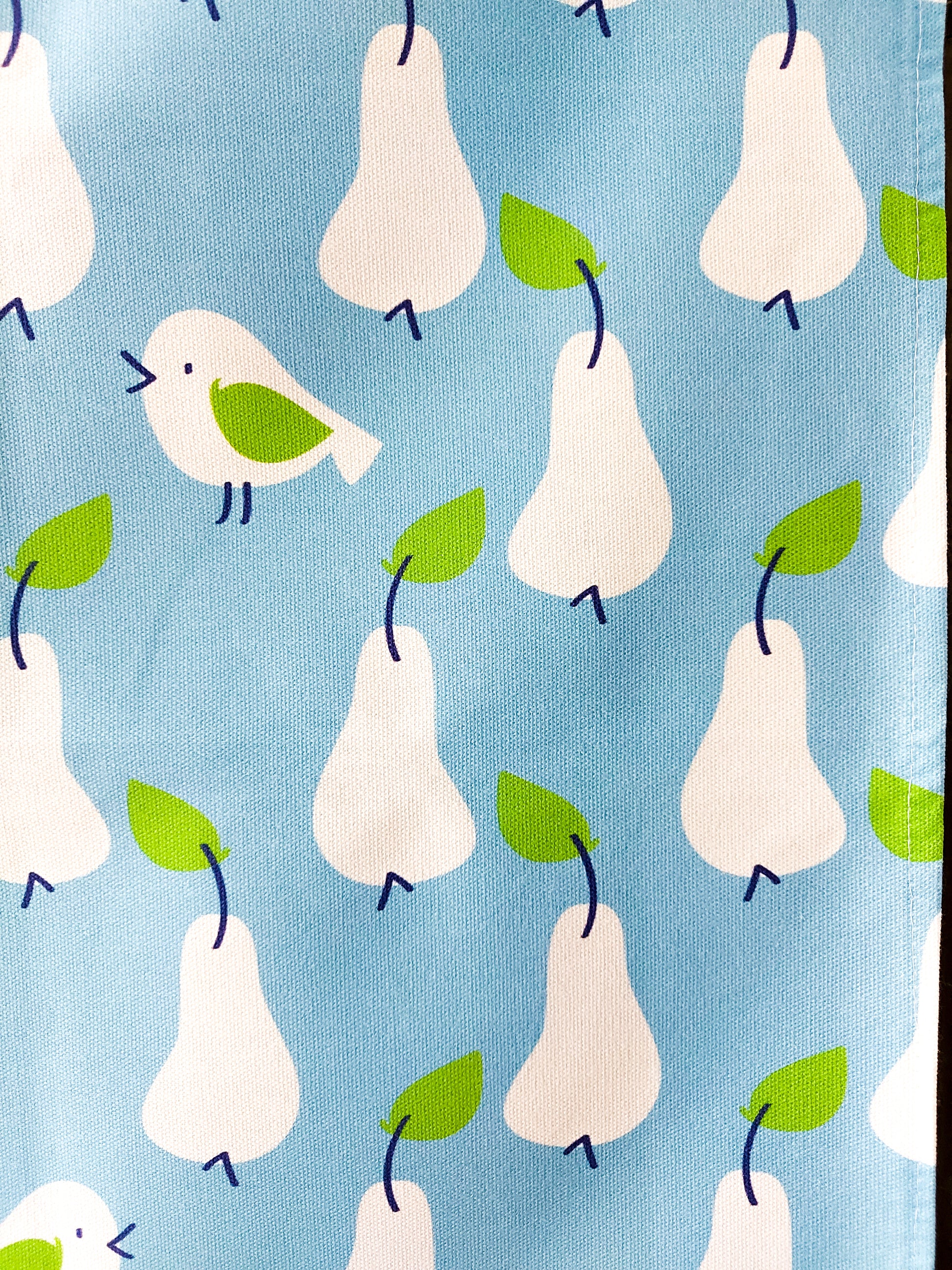 Close up photo of the Just Pears tea towel showing white pears and birds with green leaves on a light blue background