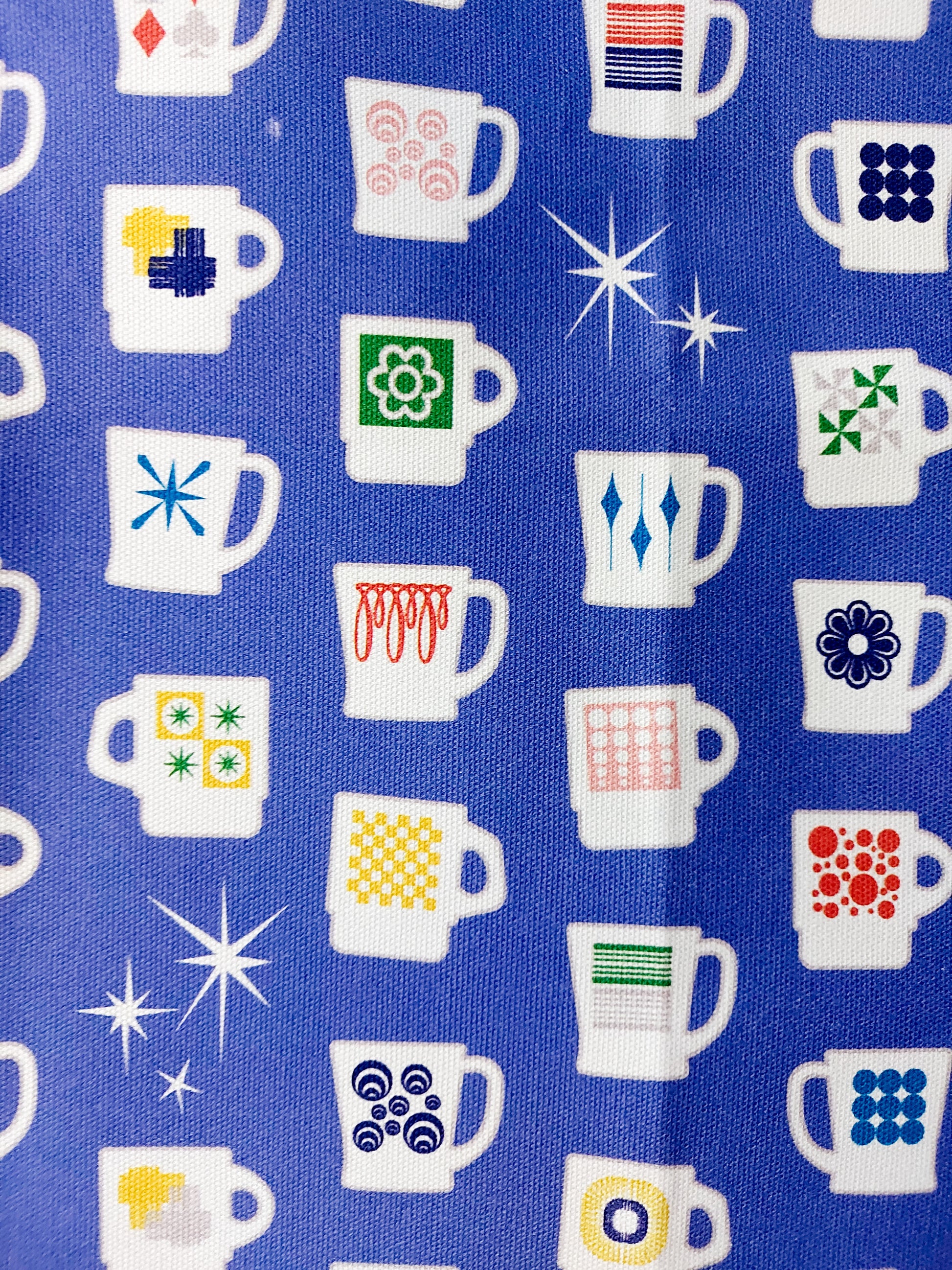 Close up photo of the Kings of Cups tea towel showing some of the cups with retro motifs, white stars and a bright blue background