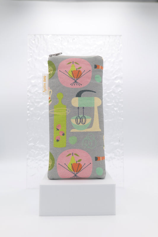 Glasses case featuring the Kitchen Kitsch design with retro-style illustrations of stand mixers, chopping boards, fruit bowls and other kitchen items in pink, green, orange and cream on a soft grey background; made from cotton canvas with a zip-top closure, padded and lined to protect lenses, handmade in Melbourne and certified Australian Made; pattern placement may vary slightly due to the handmade nature of the product.