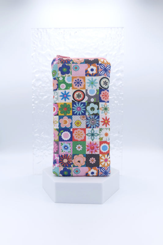 Glasses case with Les Fleurs design featuring a colourful patchwork of small square tiles, each with a small floral motif in pink, blue, green, orange, and purple; made from cotton canvas with zip top closure, padded and lined with soft cotton, handmade in Melbourne and certified Australian Made; pattern placement may vary slightly and individual items may have small quirks due to the handmade nature of the product.