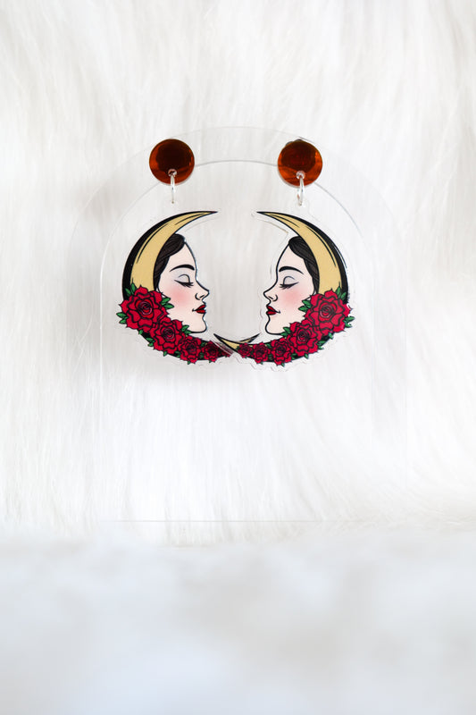 Pair of lightweight acrylic earrings in a crescent moon shape, featuring a female face and red tattoo-style roses, stainless steel posts and large accessible backs, displayed against a white background