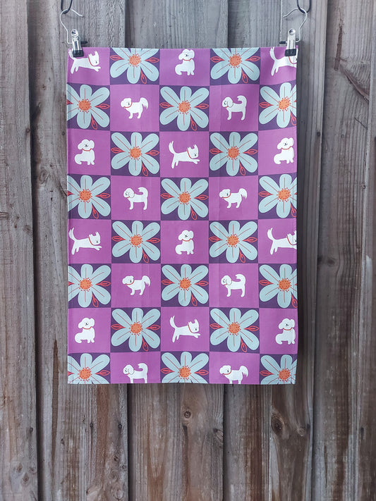 Cotton tea towel featuring a grid design with alternating white cute cartoon dog and pale blue flowers, on a purple background; displayed against a wooden fence