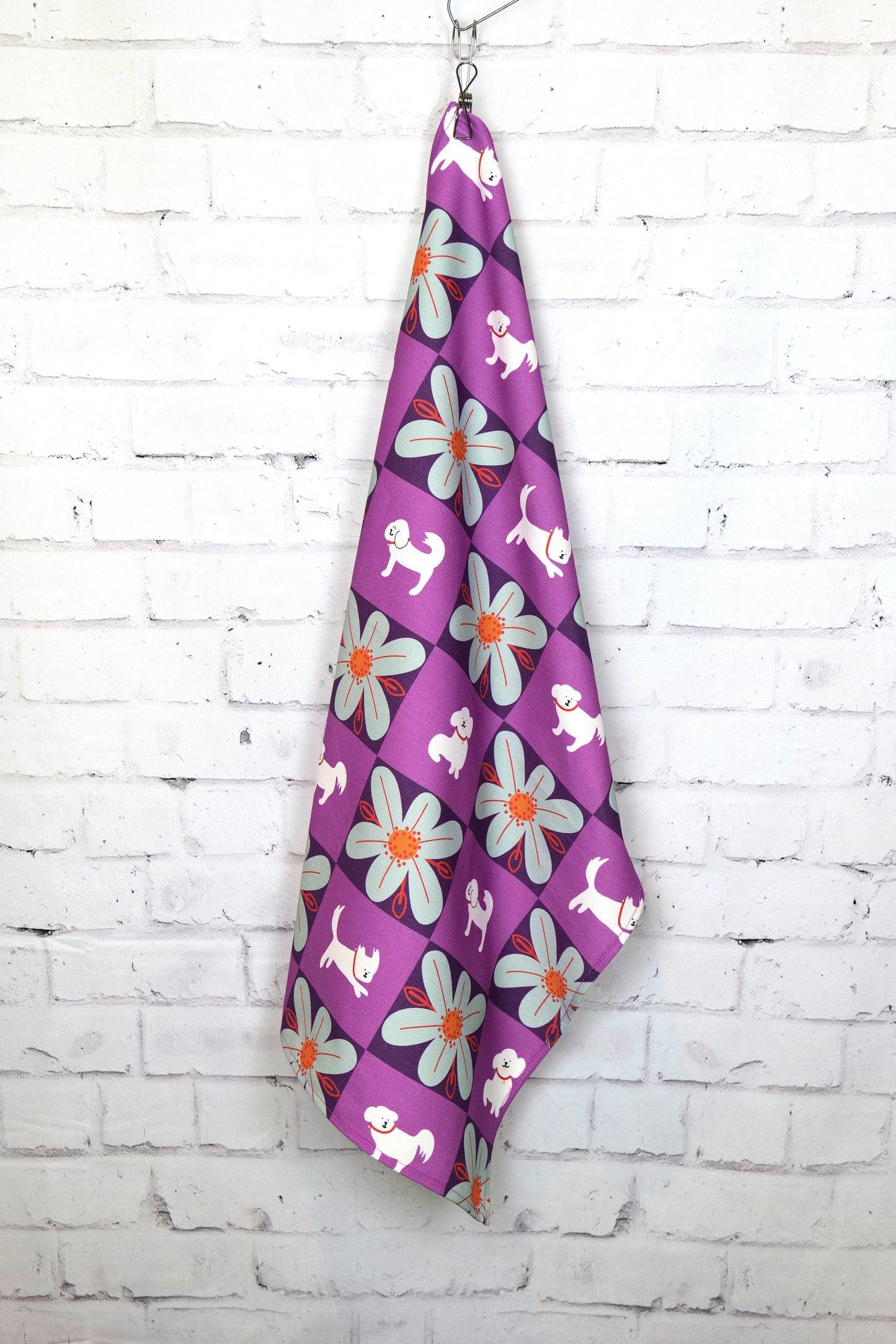 Photo of the My Hero Winky tea towel hanging by a peg against a white brick wall