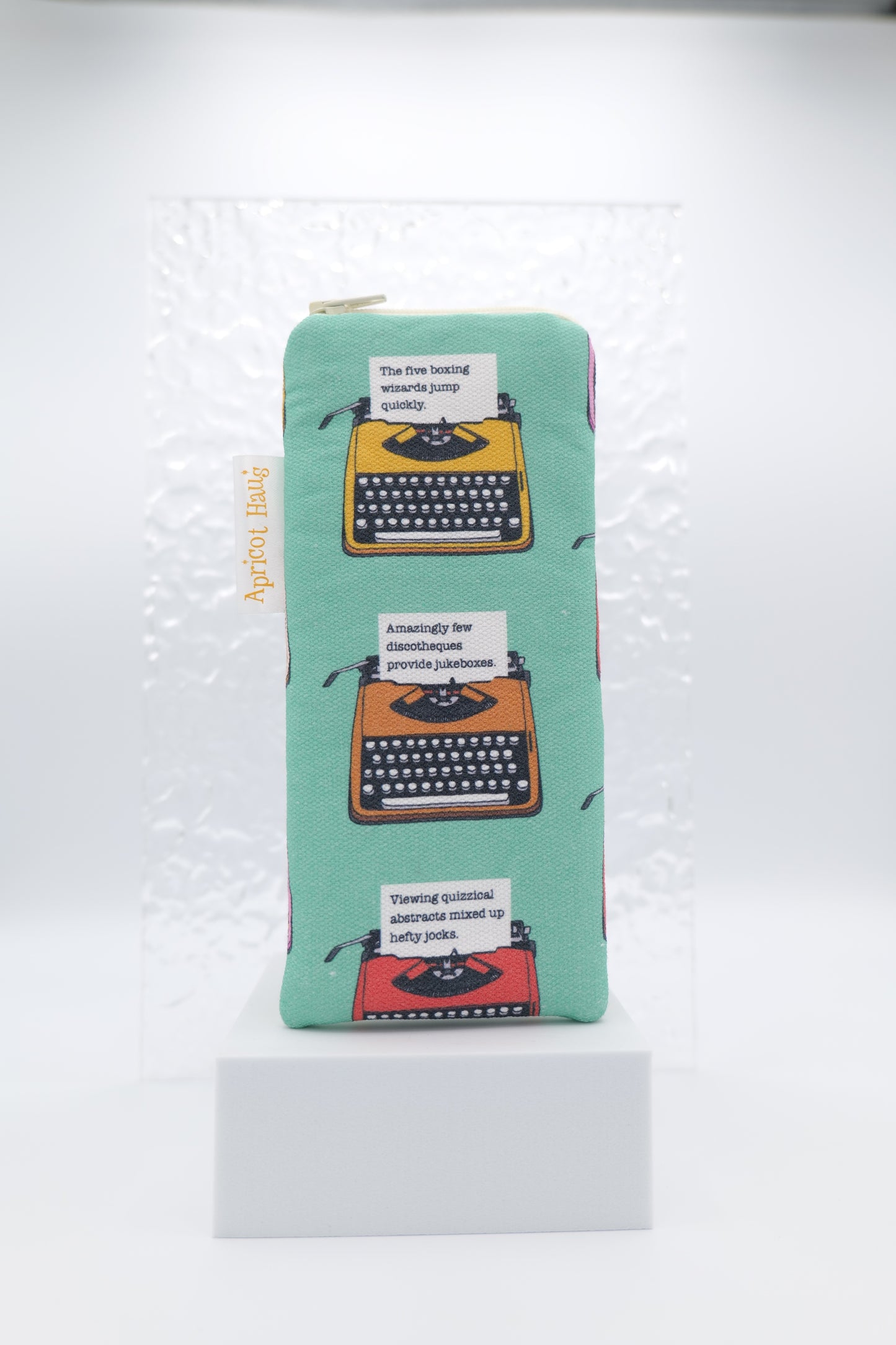 Glasses case featuring Pangram Typewriters design with illustrated vintage typewriters each typing a different pangram (sentences using every letter of the alphabet) on a soft green background; made from cotton canvas with a zip-top closure, padded and lined to protect lenses, handmade in Melbourne and certified Australian Made; pattern placement may vary slightly due to the handmade nature of the product.