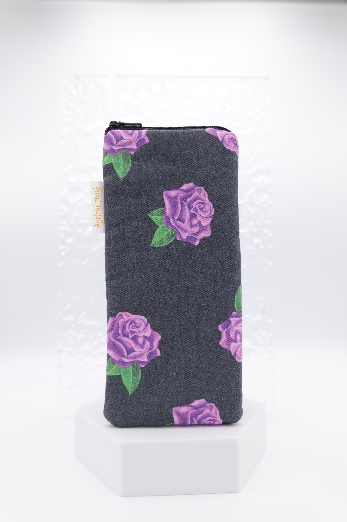 Glasses case featuring a Purple Roses design with violet rose clusters and green leaves on a dark charcoal background; made from cotton canvas with a zip-top closure, padded and lined to protect lenses, handmade in Melbourne and certified Australian Made; pattern placement may vary slightly due to the handmade nature of the product.