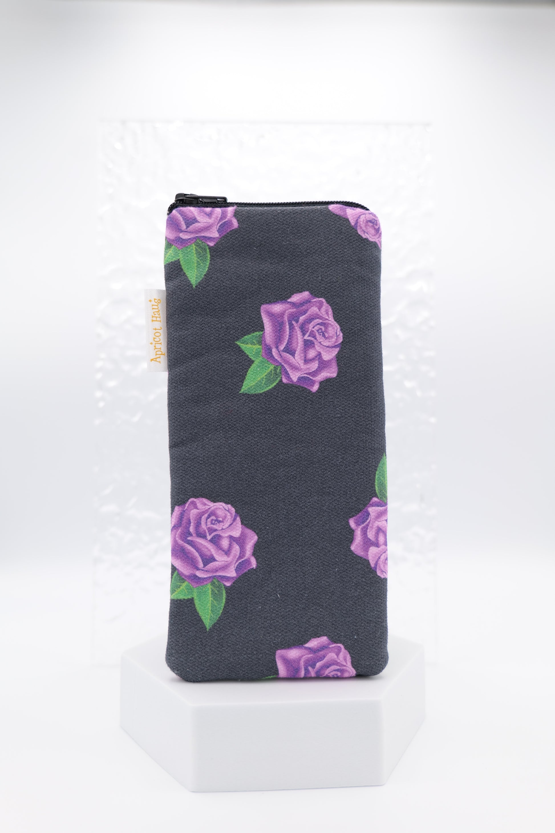 Glasses case featuring a Purple Roses design with violet rose clusters and green leaves on a dark charcoal background; made from cotton canvas with a zip-top closure, padded and lined to protect lenses, handmade in Melbourne and certified Australian Made; pattern placement may vary slightly due to the handmade nature of the product.