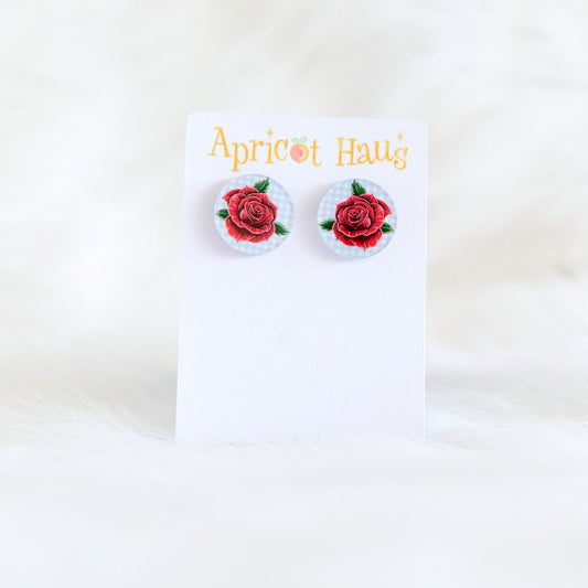 Two 2cm round stud earrings featuring a traditional style red rose on a soft blue and white check background, printed on acrylic with stainless steel posts and large accessible backs, displayed on an Apricot Haus earring card