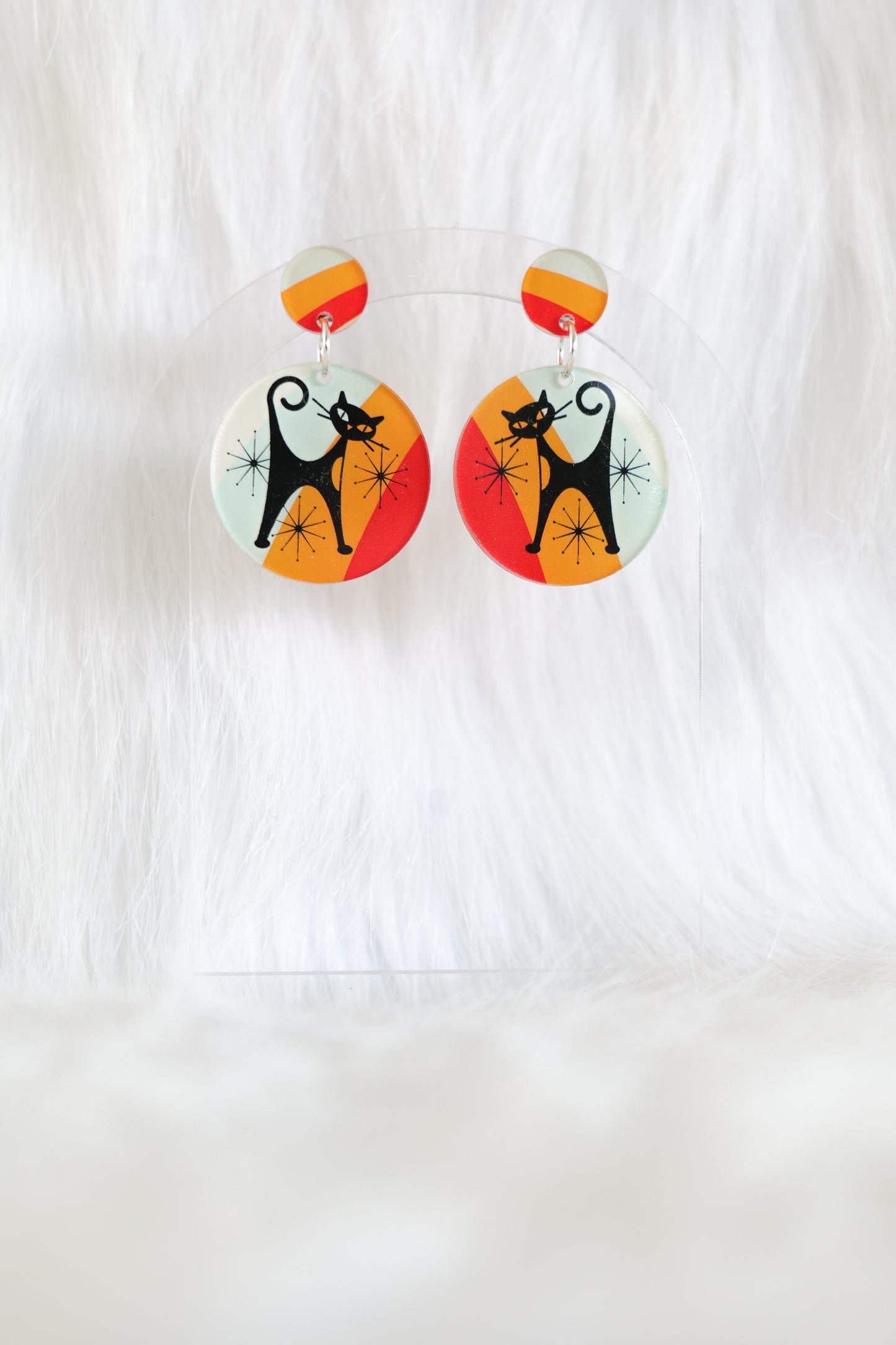 Pair of round acrylic earrings featuring atomic stye black cats with starbursts and bright coloured striped background; lightweight with stainless steel posts and large backs, designed for easier handling and visibility