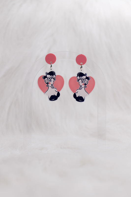 Pair of acrylic earrings with a pink circular stud and heart-shaped drops featuring a retro pin-up styled illustration of a girl with dark hair and bow; lightweight with stainless steel posts and large backs for accessibility, displayed against a white backgound 