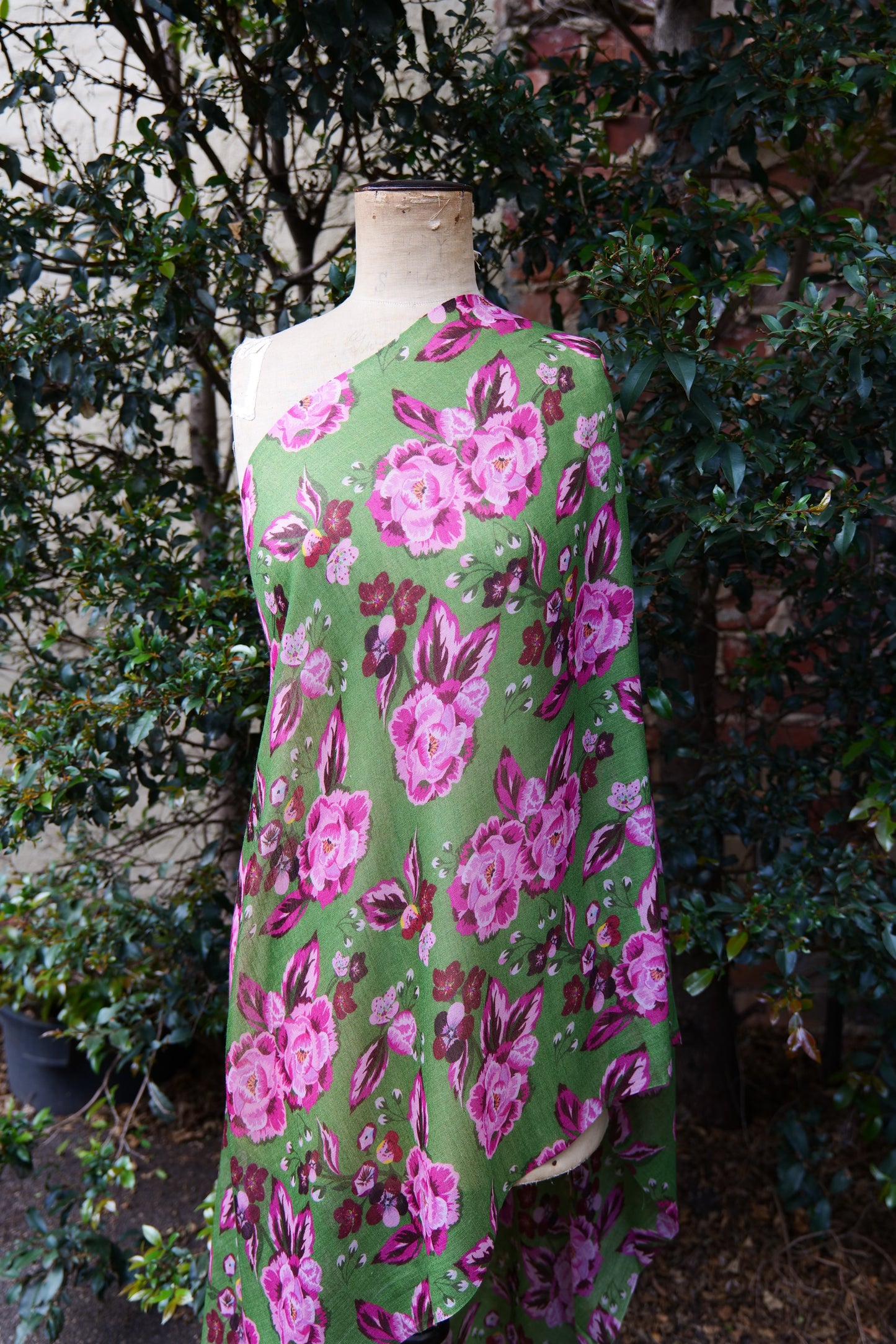 A bright green scarf with a pink toned floral design, displayed on a mannequin in front of a green tree