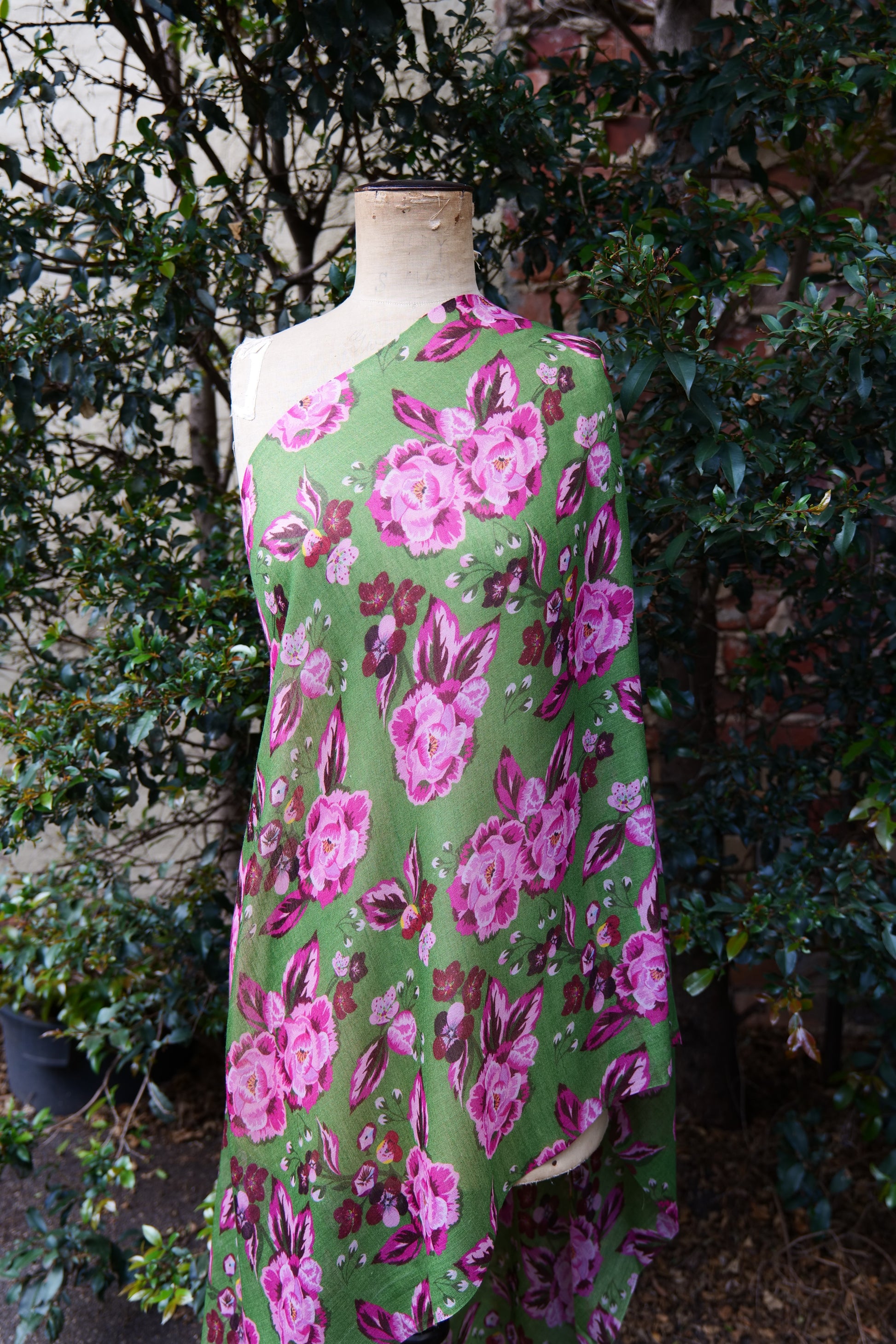 A bright green scarf with a pink toned floral design, displayed on a mannequin in front of a green tree