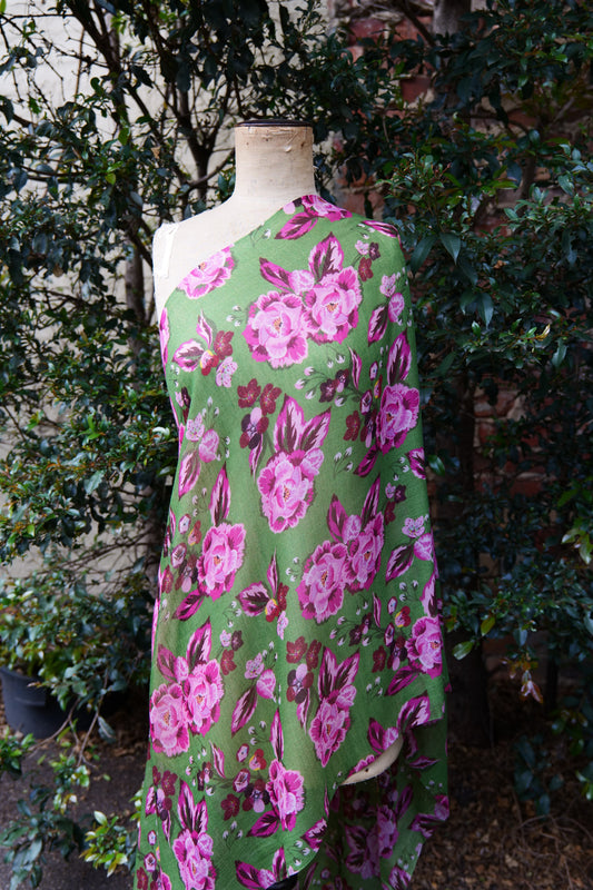 A bright green scarf with a pink toned floral design, displayed on a mannequin in front of a green tree