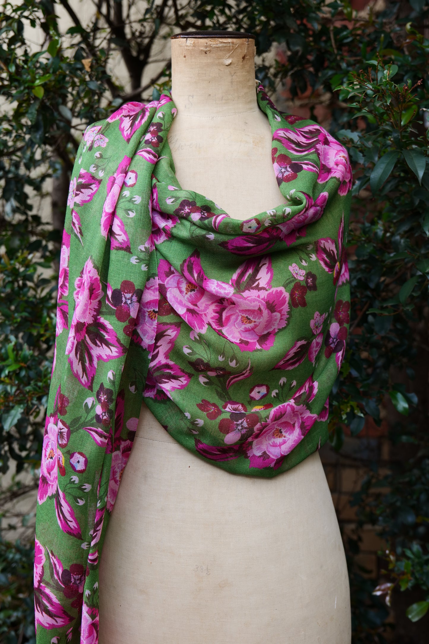 A bright green and pink floral scarf displayed on a mannequin as a loose wrap