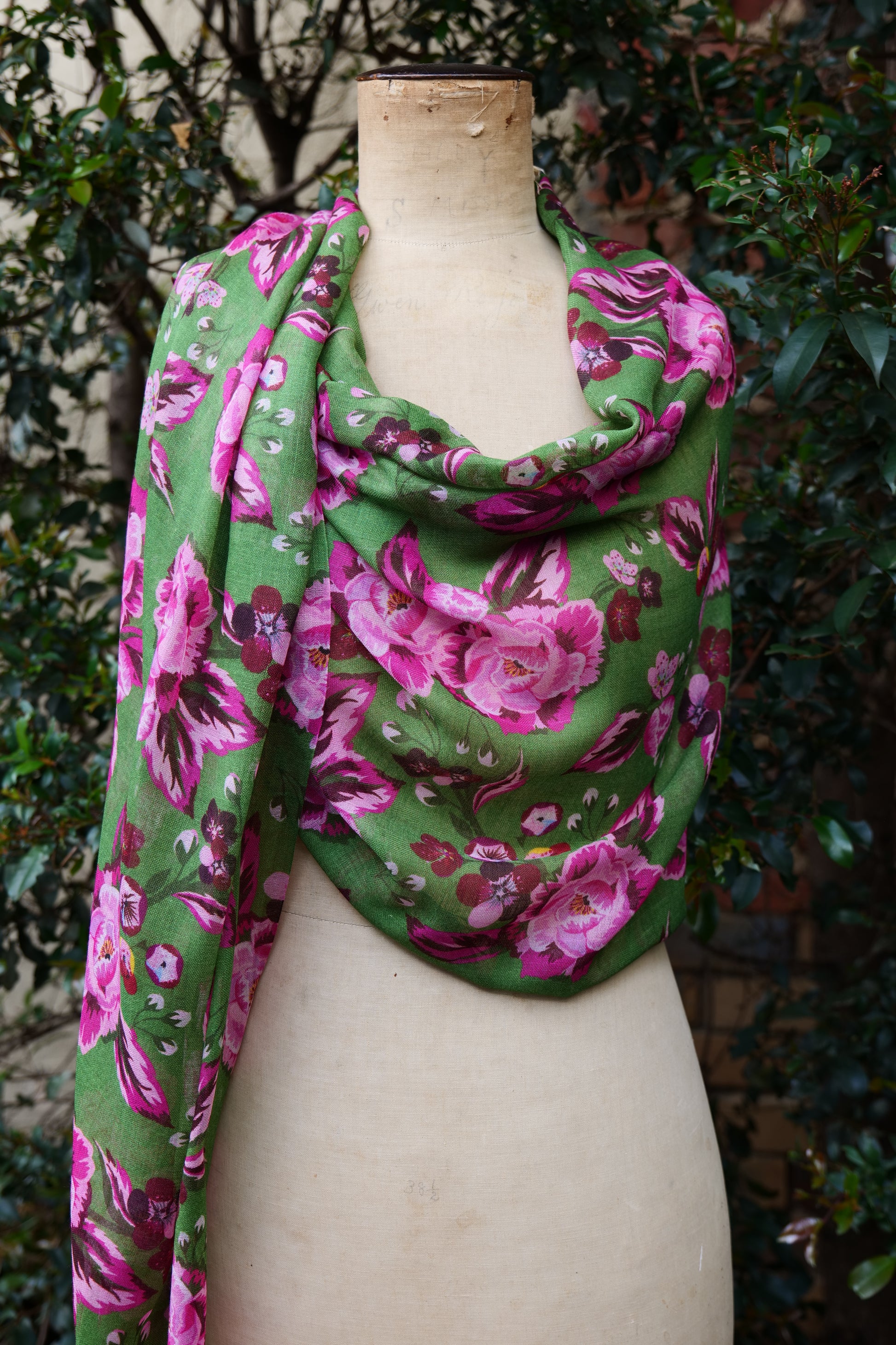 A bright green and pink floral scarf displayed on a mannequin as a loose wrap