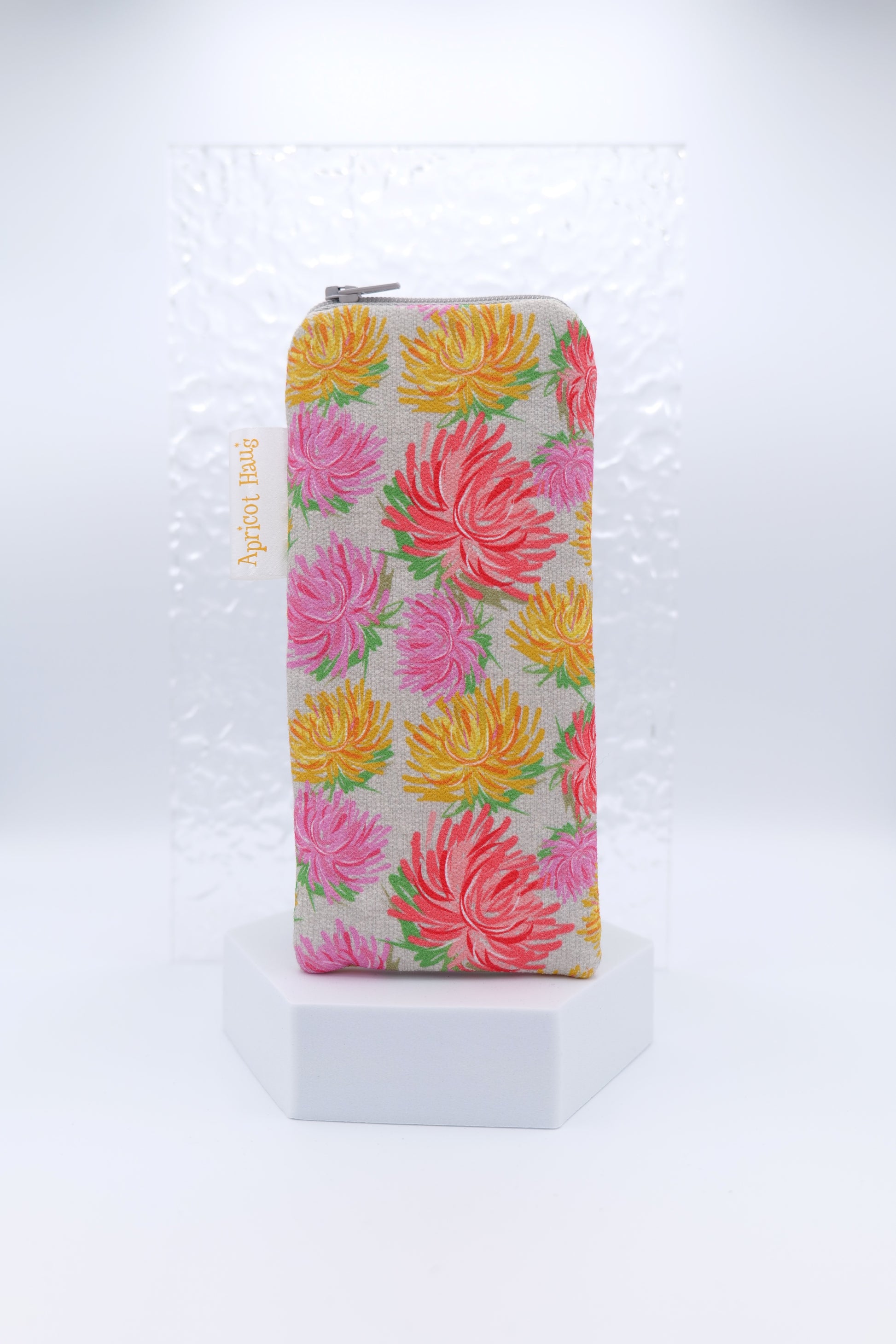 Glasses case featuring a Sketch Flowers design with hand-drawn flowers in coral, pink, and yellow on a grey-beige background; made from cotton canvas with a zip-top closure, padded and lined to protect lenses, handmade in Melbourne and certified Australian Made; pattern placement may vary slightly due to the handmade nature of the product.