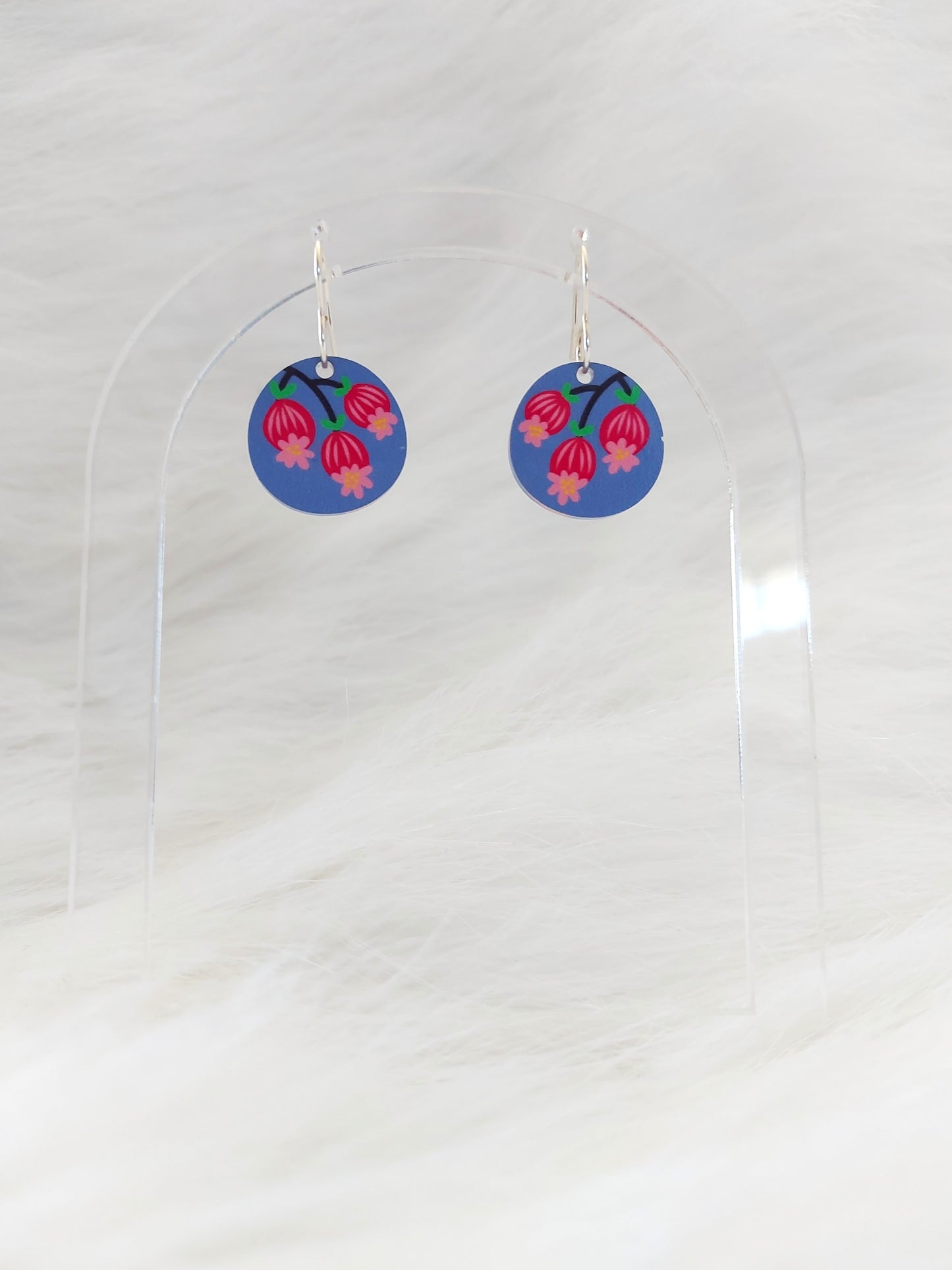 Pair of round earrings featuring three Scandinavian inspired blossoms against a blue-mauve background; printed on lightweight acrylic with stainless steel hooks, displayed against a white background