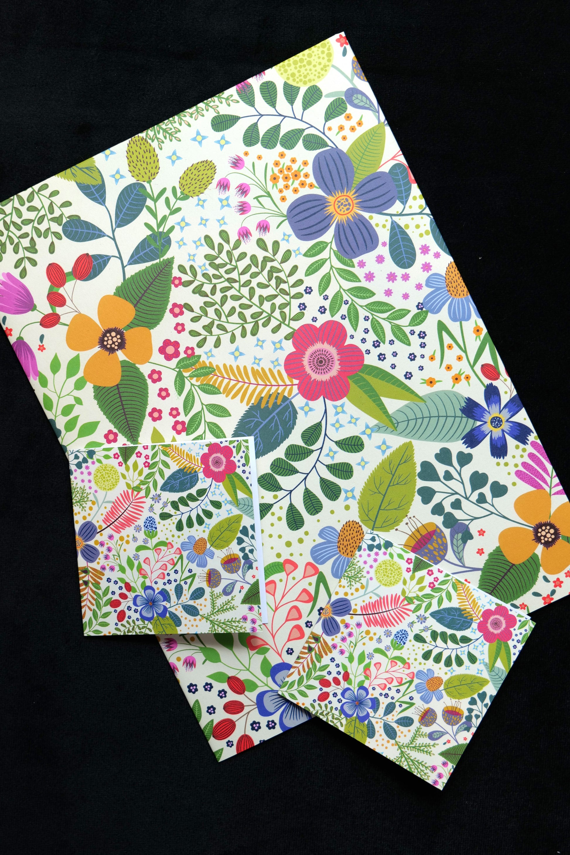 A folded piece of gift wrap and two small gift cards featuring the bright Spring Garden design, displayed against a black background