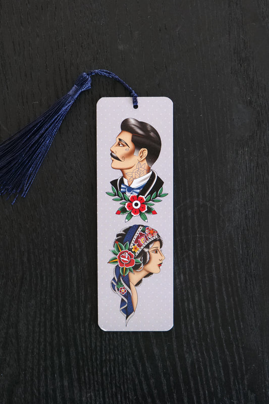 Bookmark with traditional tattoo style male and female faces, against a pale grey background with a navy tassel; sitting against a black backdrop