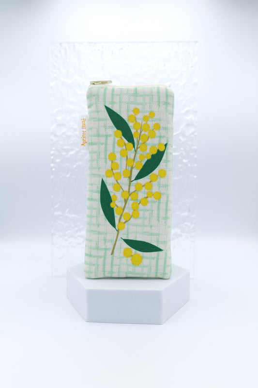 Glasses case featuring the Wattle design with a large sprig of yellow wattle blossom and green leaves set against a soft green check background; made from cotton canvas with a zip‑top closure, padded and lined to protect lenses, handmade in Melbourne and certified Australian Made; pattern placement may vary slightly due to the handmade nature of the product.